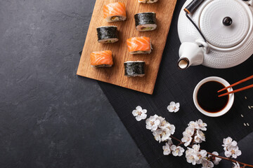 Set of sushi and maki rolls with branch of white flowers and teapot with the inscription green tea on stone table