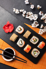Set of sushi and maki rolls with branch of white flowers on stone table
