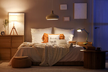 Interior of dark bedroom with glowing lamps, laptop and books on bed at night