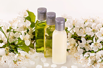 Three natural cosmetic bottles with silver caps stand among fresh white blossoms. Delicate floral setting enhances concept of organic beauty, skincare and relaxation with soft, luxurious aesthetic