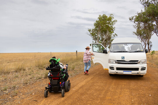 Middle aged woman and son with disability on a wheelchair with white van on road