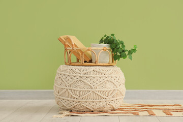 Pouf and tray with books and houseplant near green wall in room. Closeup