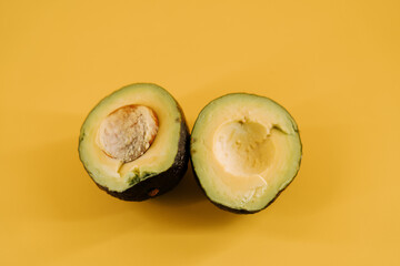 Freshly cut avocado halves with pit displayed on bright yellow background