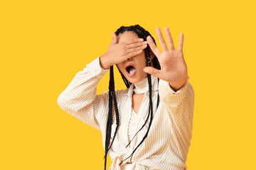 Beautiful young scared African-American woman on yellow background