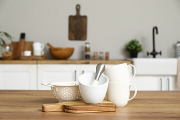 Cups, colander, board, mortar and pestle on wooden counter in kitchen