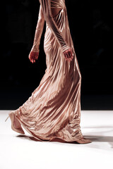 Long beige glittering dress on a female figure, stylish fashion clothing details against the black...
