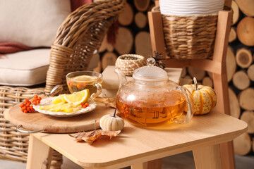 Teapot, cup of green tea with rowan, lemon and autumn decor on coffee table in room. Closeup