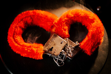 Bright orange handcuffs rest on a dark surface illuminated by soft light