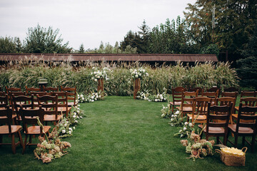 A meadow in the courtyard with a low floral arch and large wooden chairs arranged for a wedding ceremony, creating a rustic and intimate outdoor setting