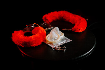 Bright red handcuffs and a condom on a dark surface create an intriguing atmosphere