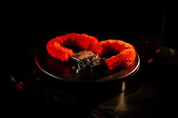 Brightly colored handcuffs with fur displayed on a dark surface under dramatic lighting