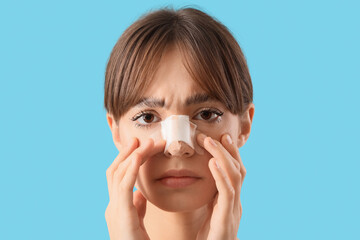 Beautiful young worried woman with bandaged nose on blue background. Plastic surgery concept