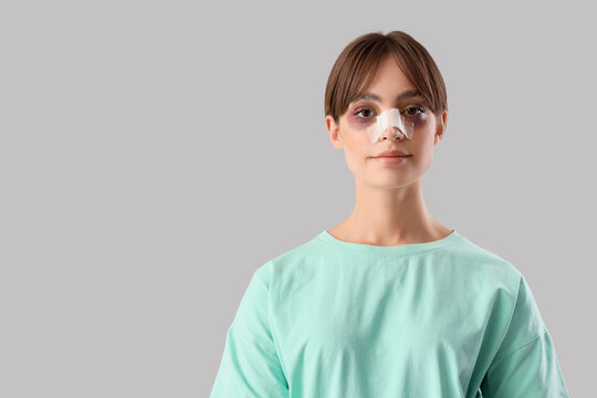 Beautiful young happy woman with bandaged nose on grey background. Plastic surgery concept