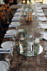 A rustic wooden table set with elegant glassware and floral centerpieces in clear vases in an event...