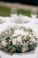 A close-up of a floral centerpiece with baby's breath and white roses on a white tablecloth in an...
