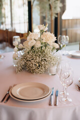 An elegant table setting for a wedding ceremony features white calla lilies, orchids, and freesia in a glass vase. Two candles in glass holders create a cozy, romantic atmosphere
