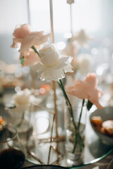 A delicate close-up captures a floral arrangement featuring white and light pink roses in small, clear glass vases on a glass table