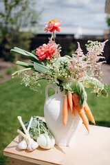 Floral arrangement with carrots and vegetables in a white vase on a table outdoors