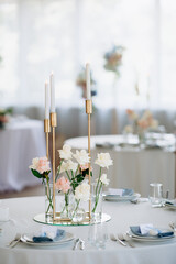 Many thin white candles in slender single candle holders burning on a banquet table in a restaurant, featuring pastel tones and a chic, minimalist atmosphere for a celebration or banquet