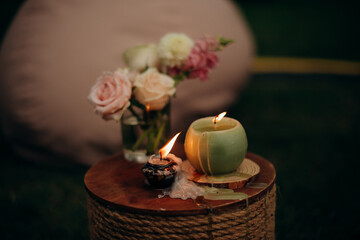 Candles burning in the dark beside flowers in a vase on a small table in an outdoor lounge area, creating a cozy and intimate atmosphere