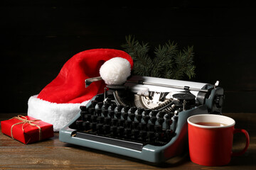 Vintage typewriter with Santa hat, Christmas tree branch, gift box and cup of tea on wooden table