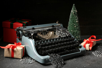 Vintage typewriter with Christmas tree, snowflakes and gift boxes on black background