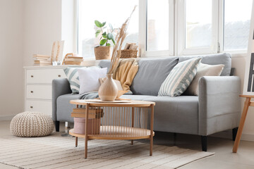Interior of light living room with grey sofa, pampas grass and books