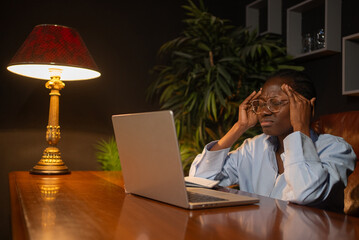 Professional African American businesswoman experiencing work-related stress, pressing temples near...
