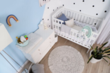 Stylish interior of modern baby's room with chest of drawers and bed, blurred view