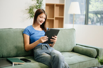 Obraz premium Young asian woman relax on comfortable couch at home texting messaging on smartphone and tablet smiling girl