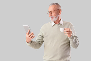 Senior businessman with tablet computer and cup of coffee on grey background
