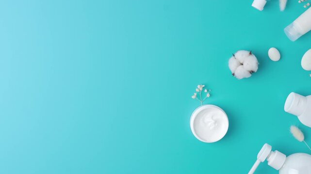 Cosmetic skin care products with flowers and wood on blue background. Flat lay, copy space