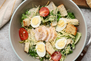 Bowl with tasty chicken Caesar salad on grey background, closeup