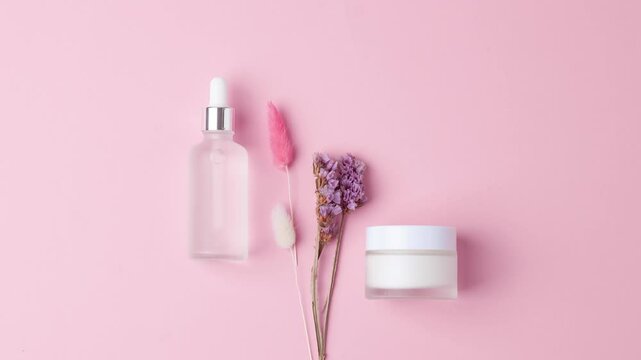 Minimal composition with cosmetic skin care products and flowers on pink background. Flat lay.