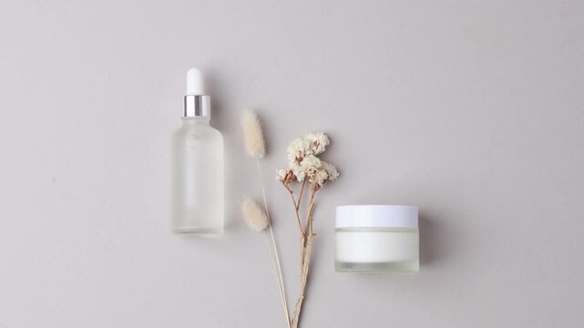 Minimal composition with cosmetic skin care products and flowers on grey background. Flat lay.