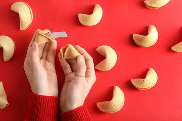 Female hands with broken fortune cookie on red background