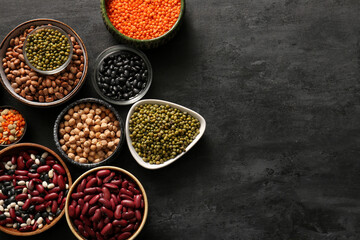 Composition with bowls of different raw legumes on dark background