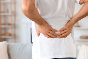 Young man suffering from back pain at home, closeup