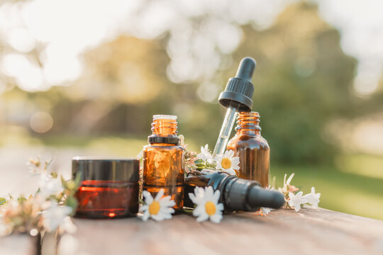 Collection of various amber essential oil bottles in natural outdoor setting with fresh flowers