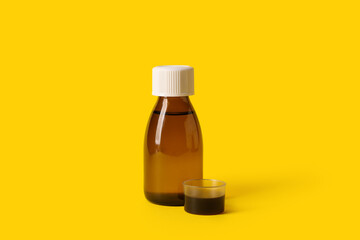 Bottle and measuring cup of cough syrup on yellow background