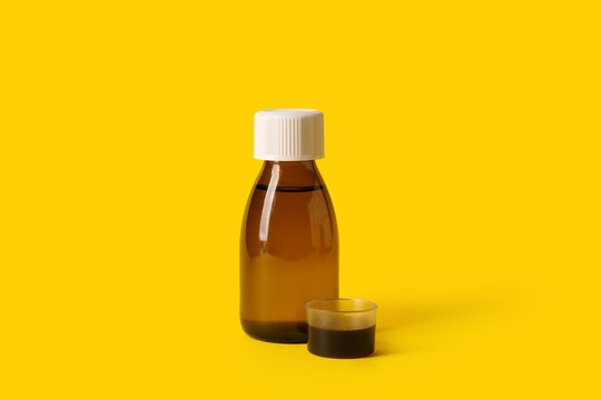 Bottle and measuring cup of cough syrup on yellow background