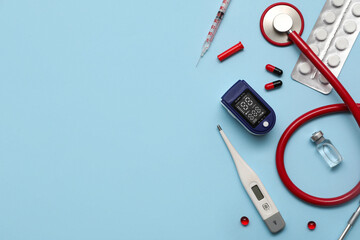 Composition with pulse oximeter, stethoscope, thermometer and medicines on blue background