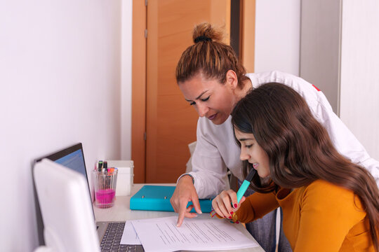 Mother guiding teenage daughter while reviewing homework at kitchen table