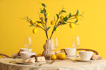 Stylish table setting decorated with beautiful lemon tree branches near yellow wall in dining room