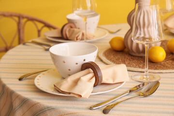 Stylish table setting decorated with fresh lemons near yellow wall in dining room