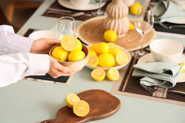 Woman decorating table setting with fresh lemons in dining room, closeup