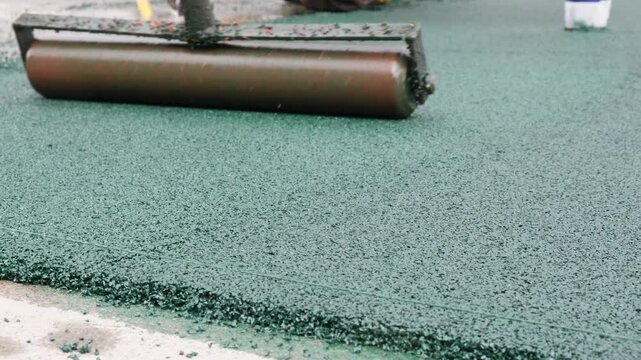 Installation of flooring on an open children's playground using polypropylene granules. Rubber crumb is rolled with a metal hand roller at the end of installation. Ethylene propylene rubber granules