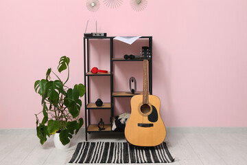 Guitar, houseplant, rack with headphones and audio system near color wall