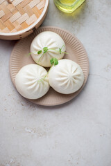 Carton plate with steamed baozi buns on a light-beige stone background, vertical shot with copy space, flat lay