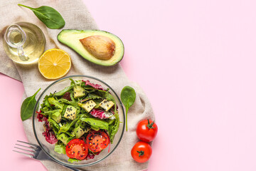 Glass bowl of tasty avocado salad with cherry tomatoes and lemon on pink background